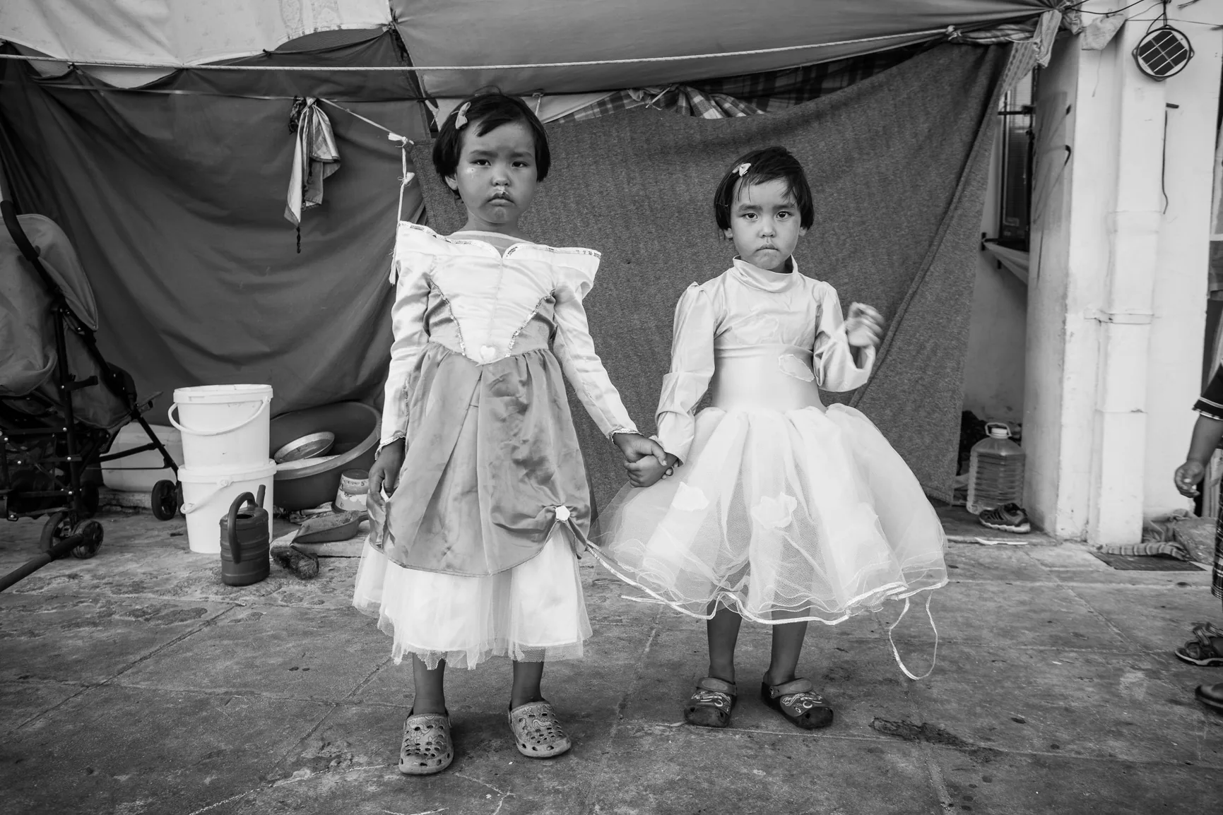 Two girls holding hands and dressed for a portrait in front of a temporary shelter.