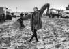 A woman in a fur coat and stockings walks barefoot through the thick desert mud